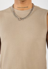 Beige ribbet topp uten ermer med rund hals, prydet med en skinnende sølvkjede som et bemerkelsesverdig detaljer.