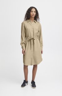 Rochie din in khaki cu închidere cu nasturi, mâneci lungi și talie legată. Asortată cu tenisi negri cu accente albe.