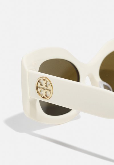 White oversized sunglasses with brown lenses, featuring a gold logo accent on the temple. Smooth plastic material with a bold shape.