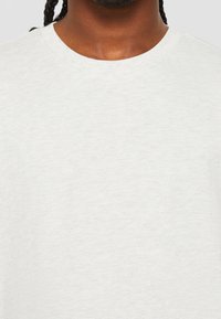 Světle šedé tričko vyrobené z měkké, texturované látky. Má kulatý výstřih a krátké rukávy. Jednoduchý, minimalistický design bez grafiky.