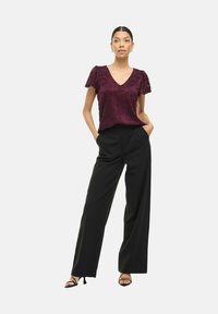 Top corto bordeaux a maniche corte con texture floreale e scollo a V, abbinato a pantaloni ampi neri a vita alta e sandali neri con cinturino.