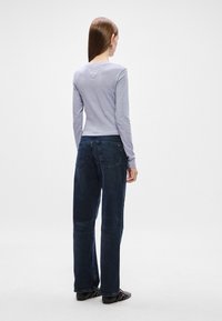 Ανοιχτό γκρι κολλητό τοπ με μακριά μανίκια και στρογγυλή λαιμόκοψη, συνδυασμένο με σκούρα μπλε φαρδιά τζιν παντελόνια. Λείο ύφασμα και απλοί σχεδιαστικοί λεπτομέρειες.