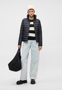 Melnā pūkaina jaka ar rāvējslēdzēju, svītrainais džemperis, gaiši zili plati džinsi un melnas masīvas zābakas. Tur melnu platu somu.