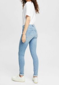 Vaqueros ajustados de color azul claro, hechos de mezclilla, con una cintura alta, cinco bolsillos y un corte clásico, combinados con una camiseta blanca y zapatillas blancas.