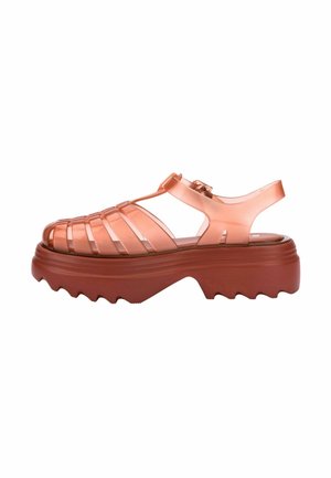 Chanclas de goma naranja translúcida con la puntera abierta, diseño de tiras entrelazadas, correa ajustable en el tobillo y suela gruesa roja con bordes irregulares.