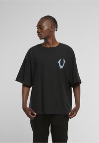 Czarny, oversize'owy t-shirt z krótkimi rękawami, z niebiesko-białym wzorem graficznym na lewej części klatki piersiowej. Gładka bawełniana faktura.