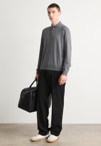 Polo grigio a maglia con colletto e tre bottoni, pantaloni larghi neri e sneakers bianche. Borsa nera con manici. Sfondo minimalista.
