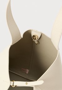 Borsa a mano in pelle texturizzata crema con apertura superiore, chiusura magnetica dorata e una tracolla larga singola vista dall'alto, che mette in risalto la fodera interna liscia.