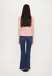 Tricou roz ajustat și blugi evazați de culoare albastră închisă. Tricoul are mâneci scurte și blugii au buzunare la spate și o evazare ușoară la tiv.