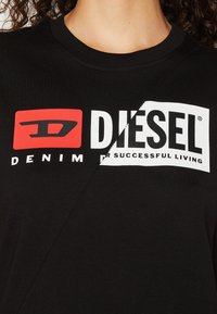 T-shirt en coton noir avec col rond présentant un grand logo Diesel rouge et blanc, incluant "DENIM" et "POUR UNE VIE RÉUSSIE."