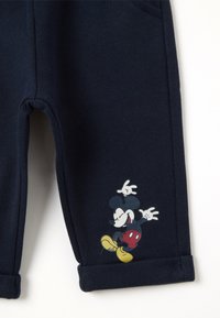 Pantalons de survêtement en coton bleu marine avec un ourlet roulé et un motif de personnage de cartoon imprimé représentant une souris stylisée en rouge, jaune et noir.
