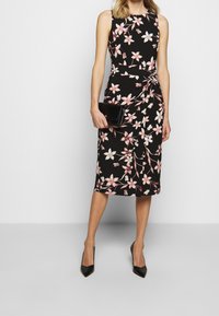 Svart blommig klänning med rosa blommönster, ärmlös design, figurnära silhuett, knälång, kombinerad med en svart clutch och svarta klackar.