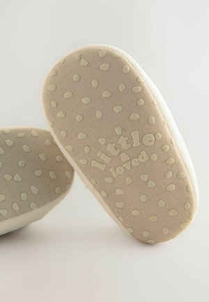 Scarpe in tessuto morbido con una base beige e suola dotata di texture a pois. Presentano il logo impresso "little & loved". La forma arrotondata migliora il comfort.