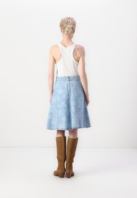 Light blue denim skirt with floral pattern, flared design, and back zipper. Paired with tall brown suede boots. White ribbed tank top.