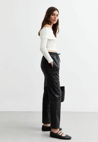 Vit off-shoulder långärmad topp i kombination med svarta faux läder byxor med dragsko och svarta platta skor med remaccent.