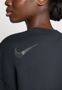 Felpa nera con una texture liscia, caratterizzata da un logo Nike riflettente sulla parte superiore della schiena e un colletto a coste.