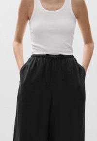 Fekete vászont nadrág, rugalmas derékkal és zsinórral, egy testhezálló fehér bordázott felsővel párosítva.