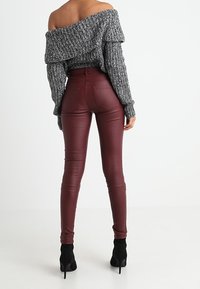 Suéter gris con hombros descubiertos y tejido texturizado; leggings de cuero sintético color burdeos; botines negros; silueta ajustada.