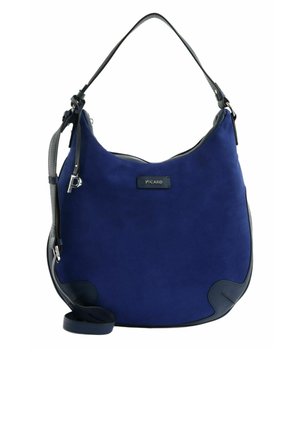 Sac à main en daim bleu avec garniture en cuir noir, une seule bandoulière, fermeture éclair et un pendentif métallique en forme de "P" sur le côté.