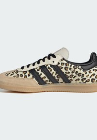 Sneaker w panterkę z beżowo-czarnym wzorem, gumową podeszwą, sznurowaniem i trzema czarnymi paskami po boku.