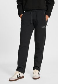 Pantalon de survêtement noir avec taille élastique à cordon, poches latérales zippées et détails de logo. Fabriqué en tissu lisse, avec une conception à jambes fuselées.