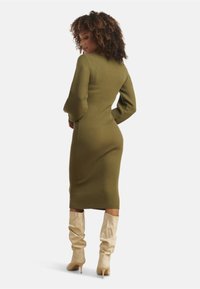 Olive ribbed midi dress featuring long sleeves and a fitted design. Worn with cream slouchy knee-high boots.