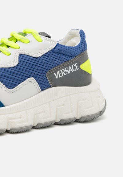 Mėlynos ir baltos sportinės kedos su tinklelio medžiaga, neoninėmis detalėmis, tekstūruotu padu ir pilkomis akcentais. "Versace" logotipas matomas šone.