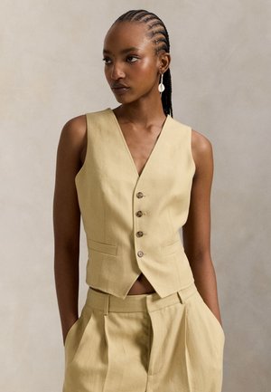 Vestă galbenă din in cu decolteu în V, cinci nasturi și buzunare laterale. Asortată cu pantaloni scurți plisati de talie înaltă în aceeași nuanță. Textură netedă.