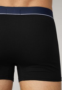 Boxer briefs neri con un elastico blu navy, caratterizzati da una texture liscia e da cuciture chiare a contrasto lungo il bordo superiore.