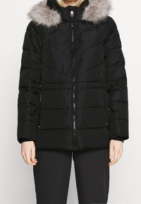 Sort puffjakke med en aftagelig grå pelsforet hætte, lynlås lukning og sidelommer med et quiltet design.