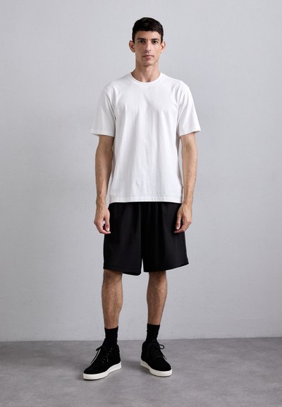 Hvit bomulls T-skjorte, kortermet; svarte treningsshorts, knelengde; svarte høyde snøresko med hvite såler; enkelt design, minimal detaljer.