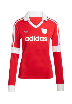 Červený futbalový dres s dlhým rukávom a bielym golierom a manžetami. Na ramenách sú tri biele pruhy a výrazne zobrazené logo "adidas".