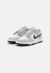 Nike Dunk sneakers in white leather with grey accents, featuring a perforated toe, grey laces, and a black rubber sole. Red Nike logo on tongue.