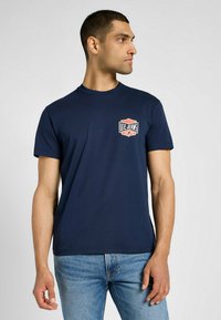 Granatowa bawełniana koszulka z okrągłym dekoltem, z małym czerwono-białym logo "Lee Jeans" na lewym piersi. Krótkie rękawy.