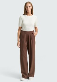 White ribbed short-sleeve sweater with a round neckline, paired with brown high-waisted wide-leg trousers and white sneakers.