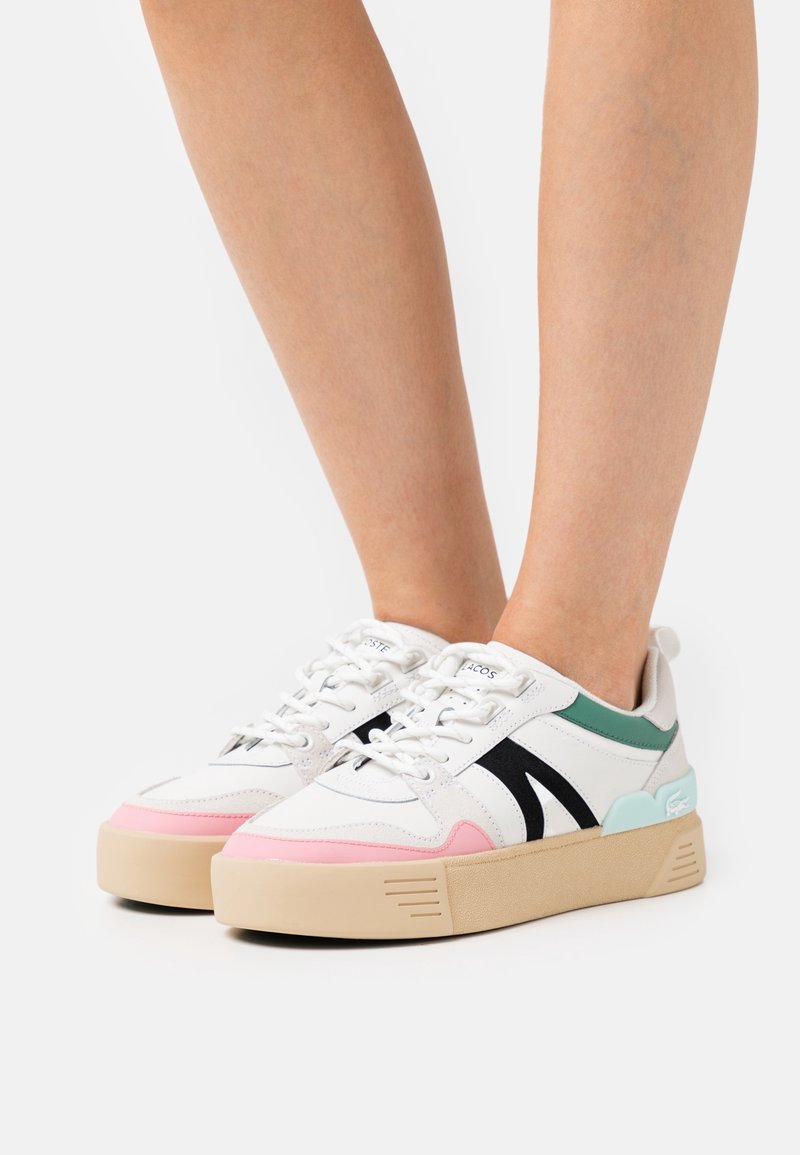 Baskets blanches basses avec des accents rose, noir, vert et bleu clair, portées sur des jambes nues, avec des semelles épaisses beige et des lacets blancs.