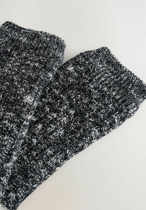 Strikkede benvarmere i sort og hvid meleret mønster, med ribbet struktur og elastisk manchet for en tætsiddende pasform.