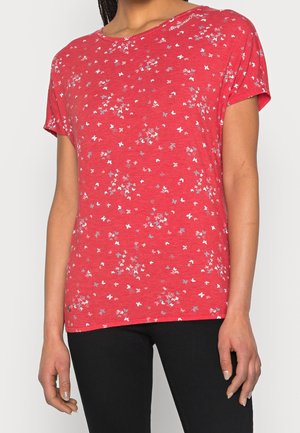 Woman wearing a red short-sleeve t-shirt with small white and gray butterfly patterns, paired with black pants against a plain background.