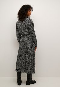 Robe à manches longues imprimée noir et blanc avec une taille cintrée, une jupe fluide et un col, associée à des bottes noires montantes.