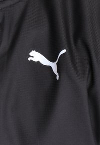 Tissu noir texturé avec une silhouette blanche d’un logo puma sautant centrée sur la surface.