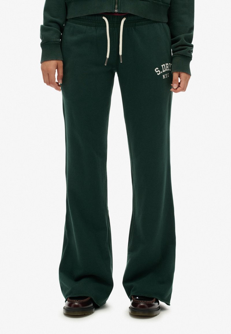 Pantalones de chándal acampanados de color verde oscuro con cintura ajustable mediante cordón, que presentan texto de logotipo en blanco en la cadera izquierda y una textura de tela suave y lisa.