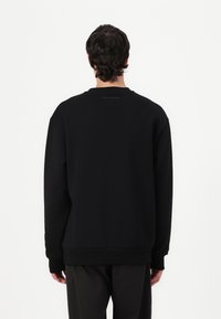 Felpa nera con maniche lunghe, scollatura tonda e polsini a coste. Tessuto liscio, marchio minimo sul colletto, vestibilità comoda.