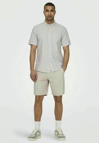 Chemise à manches courtes à boutons avec un motif rayé dans des couleurs claires, associée à un short beige et des baskets grises avec des accents crème.
