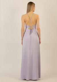 Maxikleid aus lilafarbener Satin mit überkreuzten Rückenriemen und Schnürdetails. Die glatte Textur und die fließende Silhouette unterstreichen das elegante Design.