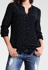 Navy long-sleeve blouse with a V-neck and white and red star-like patterns. Soft fabric, relaxed fit, paired with distressed blue jeans.