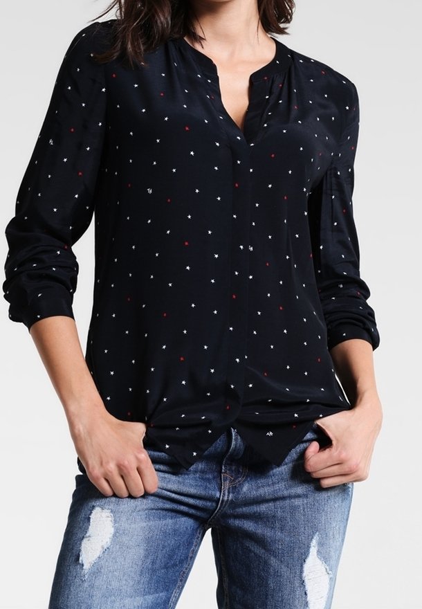 Navy long-sleeve blouse with a V-neck and white and red star-like patterns. Soft fabric, relaxed fit, paired with distressed blue jeans.