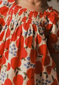 Rød og hvid kjole med smocket halsudskæring, prydet med et frugt mønster af røde æbler og blå bær, lavet af letvægtsstof.