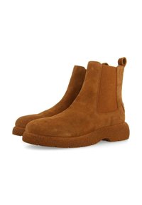 Bottes chelsea en daim marron avec des panneaux élastiques sur les côtés et une semelle en caoutchouc texturé. Dotées d'une languette à l'arrière pour un enfilage facile.