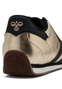 Guldmetallisk sneakerhälla med svart krage, brun texturerad sula och broderad bi-logotyp på baksidan.