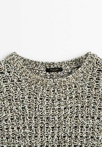 Gros plan du col d'un pull en maille texturée noir et blanc avec une petite étiquette noire à l'intérieur du col.